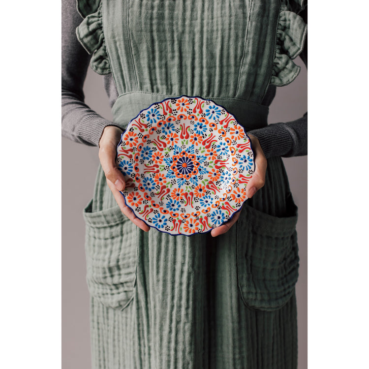 A woman holding an Heirloom Evani plate wearing a Willow green Ada apron.