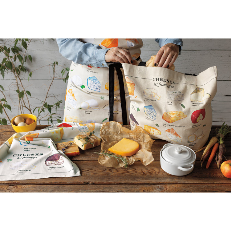 A woman wearing a Now Designs Les Fromages apron with cheese on it and filling a tote bag with a Les Fromages cheese design.