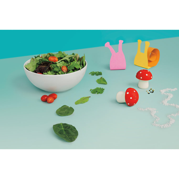 A bowl of salad next to Danica Jubilee Toadstool salt and pepper shakers shaped like mushrooms.