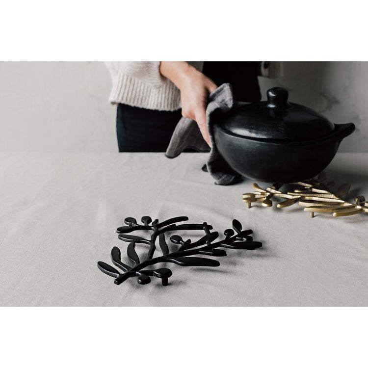 A woman placing a black teapot onto an Heirloom Matte Black Branch Metal Trivet.