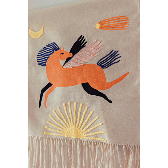 A detail shot of Astral embroidered wall art by Danica Studio featuring a pegasus horse and a sun.