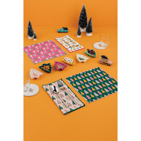 A set of cocktail napkins, Christmas tree shaped pinch bowls, and round soak up coasters from the Glitzmas collection by Danica Jubilee on an orange background.