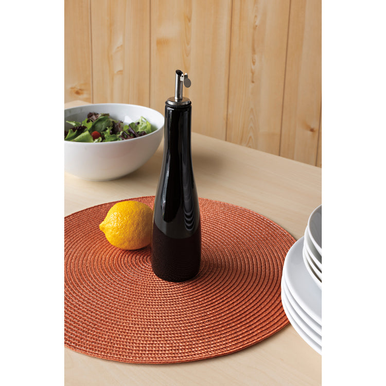 A black Now Designs cruet on a rust orange round Disko placemat.