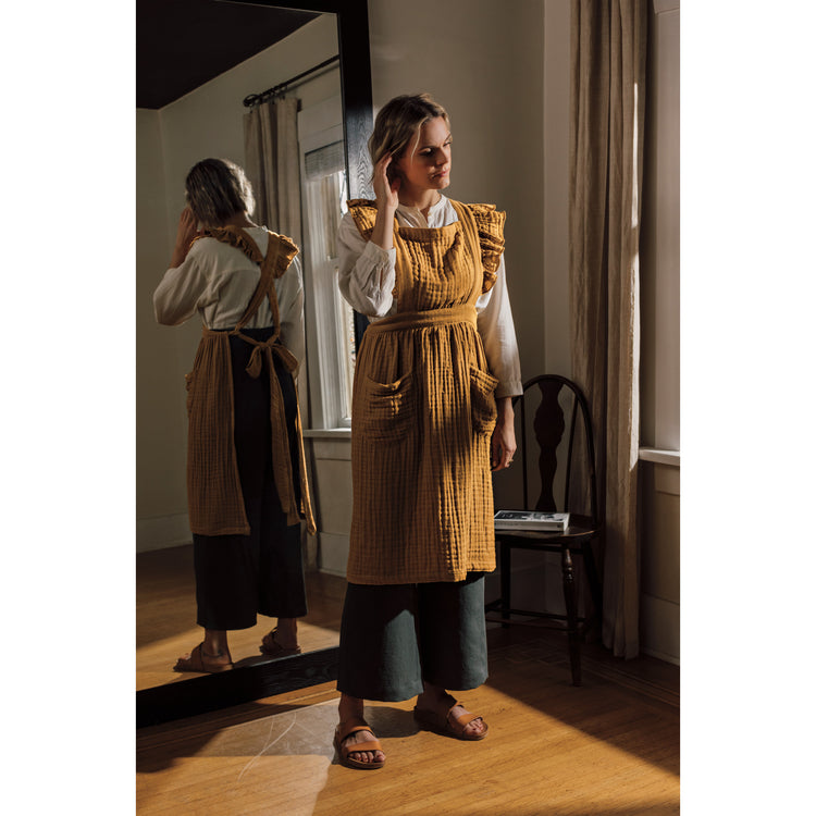 A woman in a yellow Heirloom Ada Apron standing in front of a mirror.