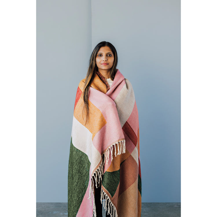 A woman is wearing a colorful Formation Prism throw blanket by Danica Studio around her shoulders.