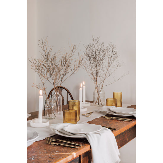 A wooden table with Heirloom Provence dinnerware and Glimmer napkins on it.