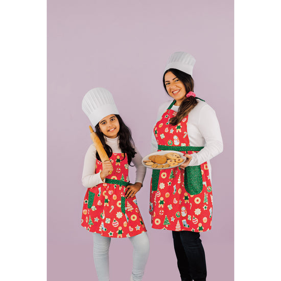 A girl and a woman in matching Christmas Maisie and Minnie Aprons with a Cookie Exchange design on them.
