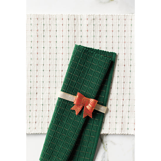 A green Now Designs ribbed placemat with copper tinsel wrapped in a red Christmas bow on top of a natural ribbed table runner with red and green tinsel.