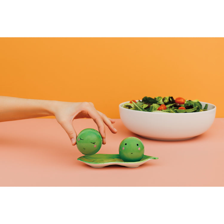 A bowl of salad next to Danica Jubilee Funny Food salt and pepper shakers shaped like green peas in a pod.