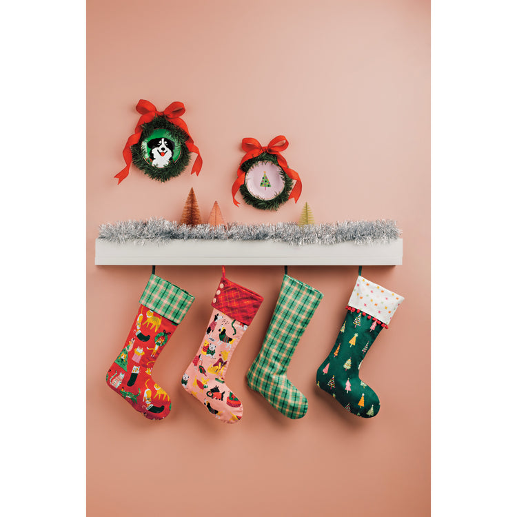 Danica Jubilee Christmas Stockings and appetizer plates with Christmas dogs on them hanging on a pink wall.