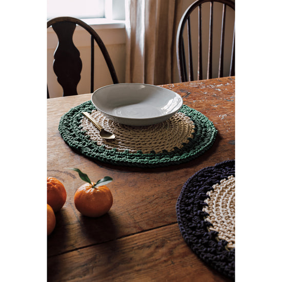 Heirloom woven Aura Placemats in Jade green and Midnight blue on a wooden table.