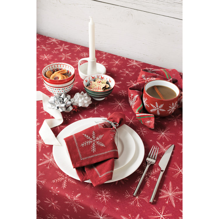 A Christmas table setting with a red Snowflakes tablecloth, napkin, latte mug, and stamped holiday bowls.