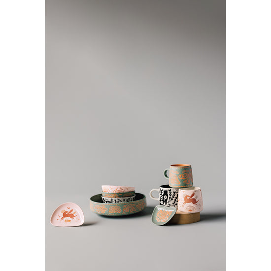 A set of Imprint plates, bowls, cups, and shaped dishes by Danica Studio on a grey surface.