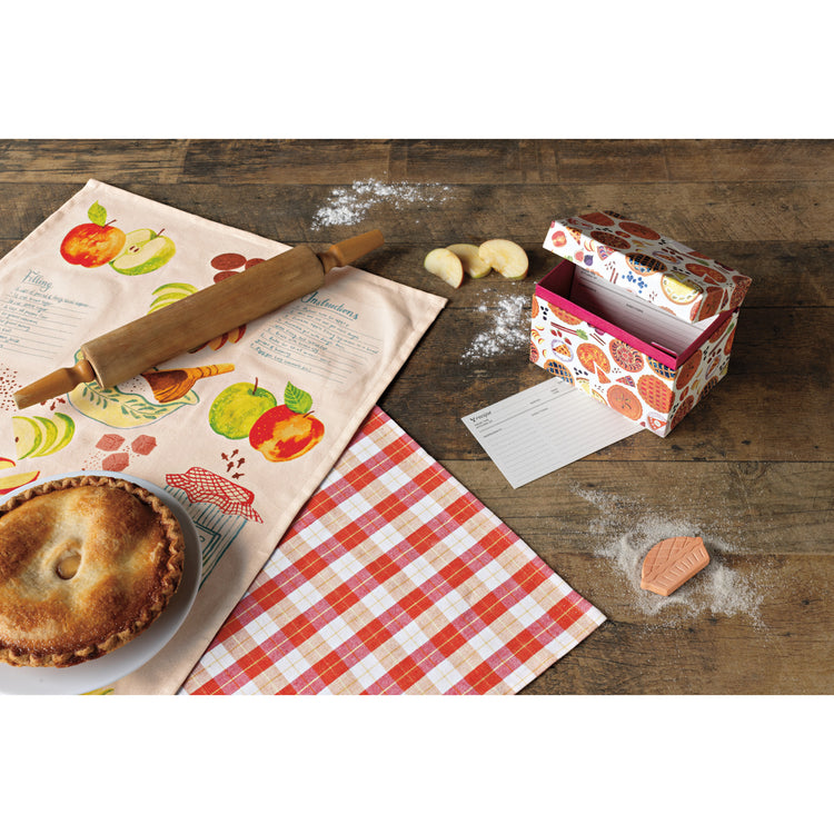 A table with a set of two Now Designs printed dishtowels with a Sweet as Pie design and a recipe box with a pie print on it and recipe cards inside. There is a pie and rolling pin on the dishtowels.