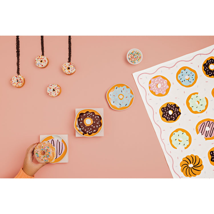 A hand reaching to place a dessert donut on a donut shaped dish by Danica Jubilee. There is also a dishtowel with donuts printed on it.