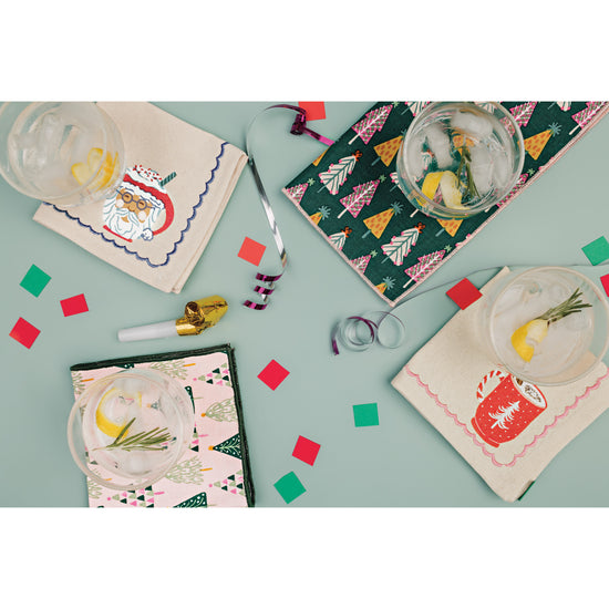 A set of Danica Jubilee printed cocktail napkins with illustrations of Christmas trees and hot drinks printed on them.