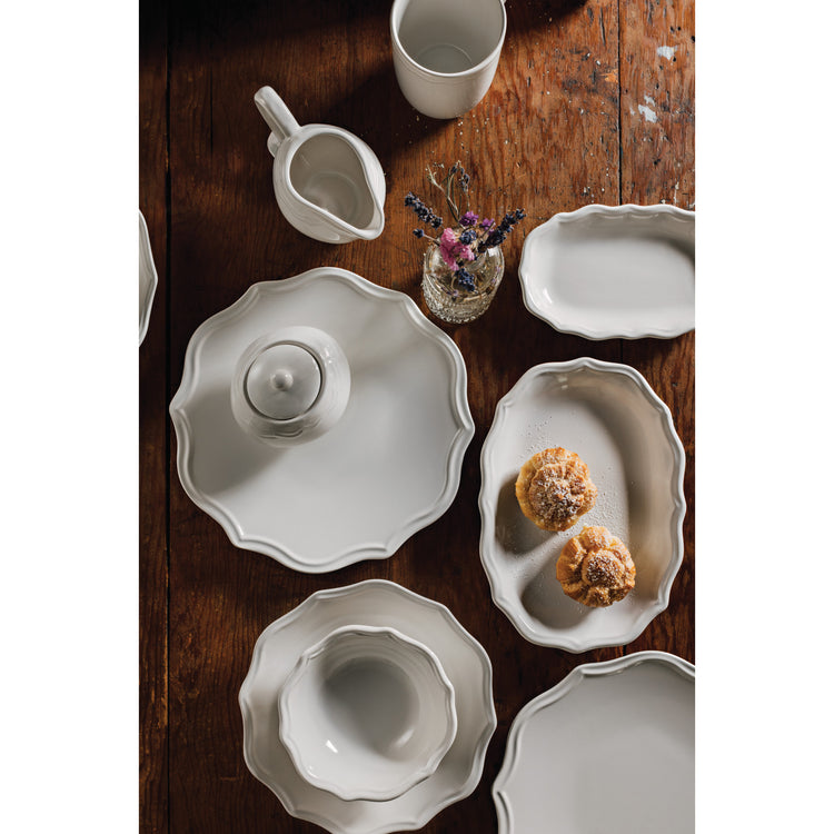 A set of Heirloom ivory Provence plates, platters, bowls, mugs, sugar pots, and creamers on a wooden table.