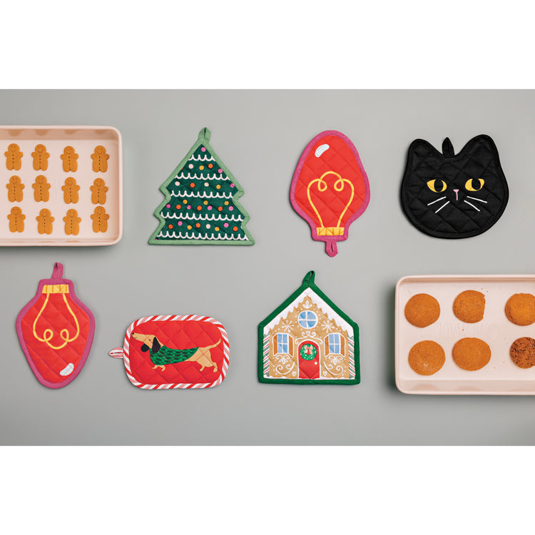 A collection of Danica Jubilee shaped potholders, including a Christmas tree, a light bulb, a Halloween black cat, a dog, and a gingerbread house.
