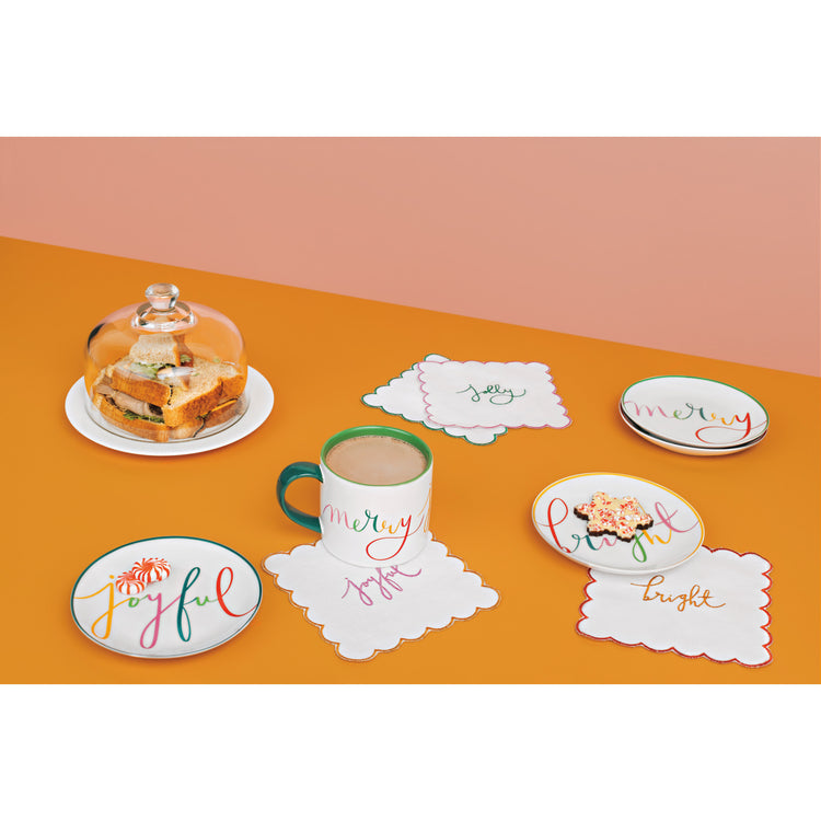 A set of plates, cups, and a mug from the Merry Everything Collection by Danica Jubilee with writing on them.