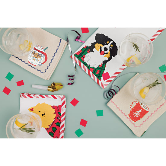 A set of Danica Jubilee printed cocktail napkins with illustrations of Christmas dogs and hot drinks printed on them.