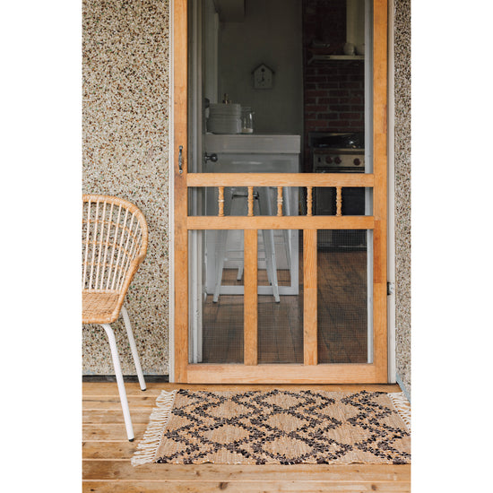 A wooden door with a Heirloom Tetra Leather Chindi Rug and a wicker chair.